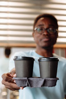Close-up of a man holding two takeout coffee cups in a cozy cafe environment.