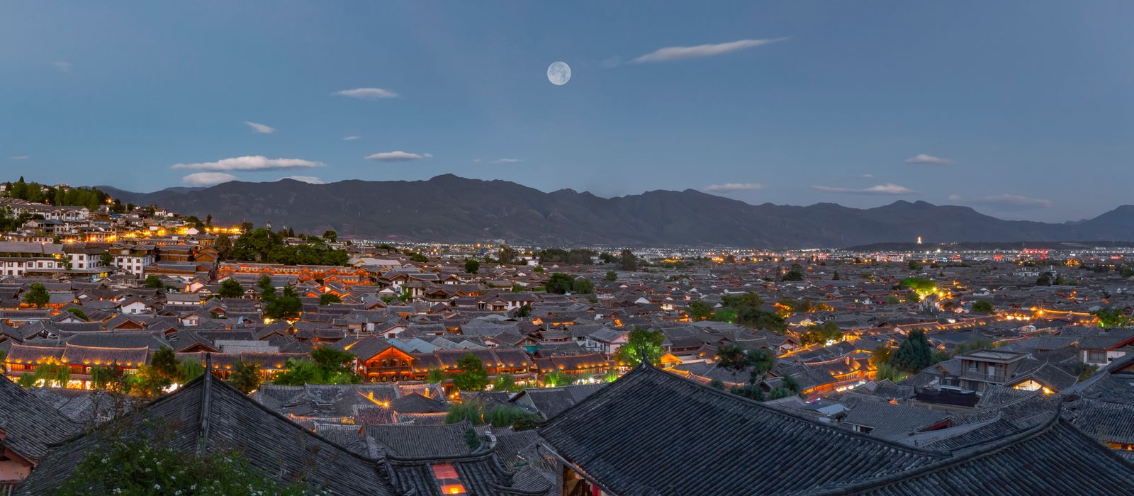 Discover the mesmerizing twilight view of Lijiang Ancient Town with traditional rooftops and mountains. — flights from Hong Kong to Lijiang