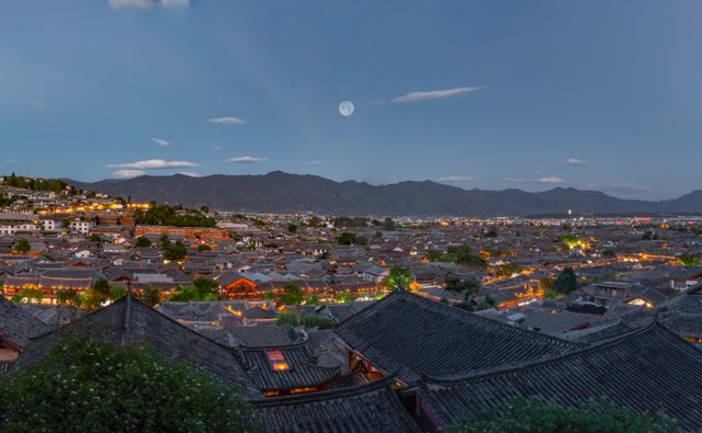 Discover the mesmerizing twilight view of Lijiang Ancient Town with traditional rooftops and mountains.