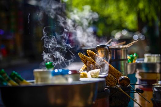 Close-up of grilled corn with steam rising on a street vendor setup, vibrant and delicious.