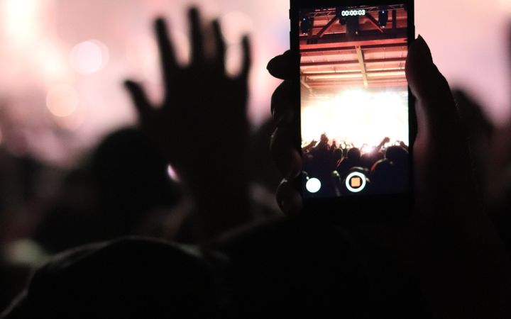 A person recording a live concert on their smartphone amidst a lively crowd.