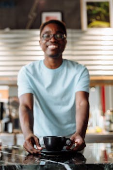 Friendly barista presenting a cup of coffee at a modern café counter, creating a welcoming atmosphere.