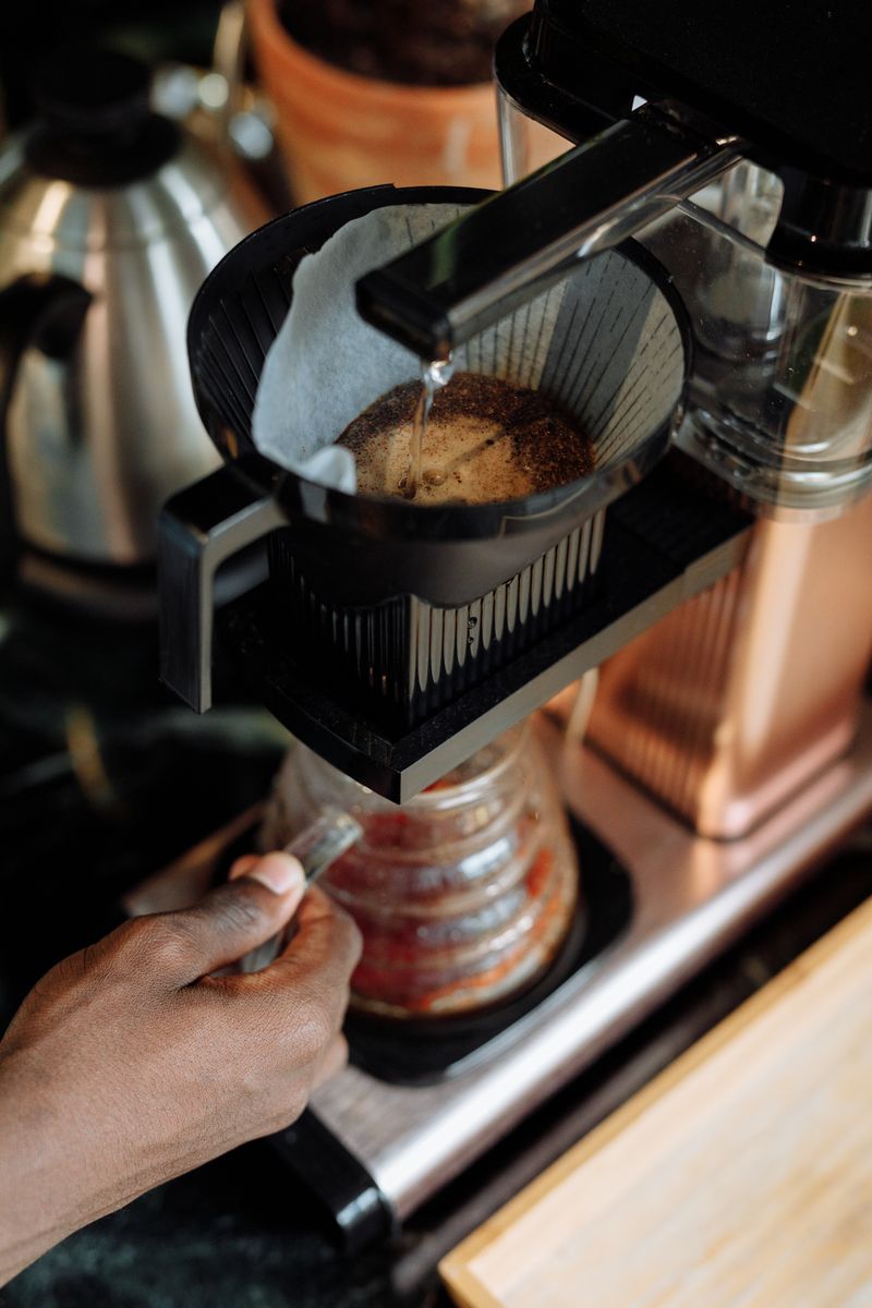 Hand pouring hot water from a kettle over coffee grounds in a filter dripper