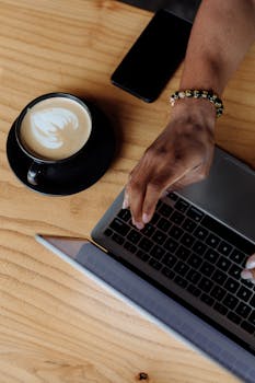 High-angle view of a person typing on a laptop with coffee nearby.