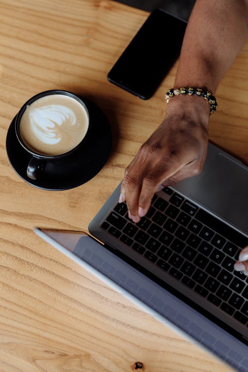Free Person Typing on a Laptop Beside Cellphone and Latte Stock Photo