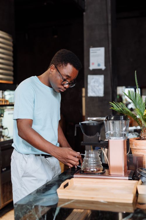 Free African American barista attentively brewing coffee in a modern cafe setting. Stock Photo