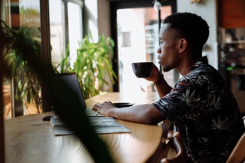 Free Adult man enjoying coffee while working on laptop in a cozy cafe. Perfect for lifestyle and work from home themes. Stock Photo