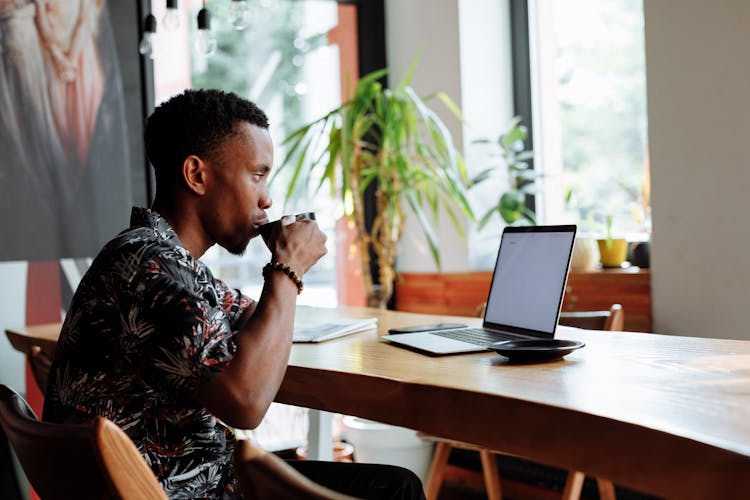 A Man In Printed Shirt Drinking Coffee While Looking At The Screen