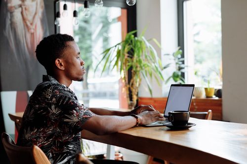 Free Side view of a man working on a laptop with a coffee in a bright cafe setting. Stock Photo