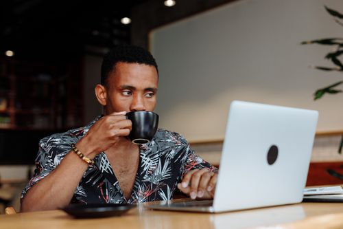 Free A man sipping coffee while working on a laptop in a cozy cafe. Stock Photo