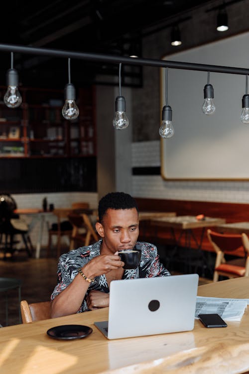 Free Man Sitting at Table with Laptop Drinking Coffee Stock Photo