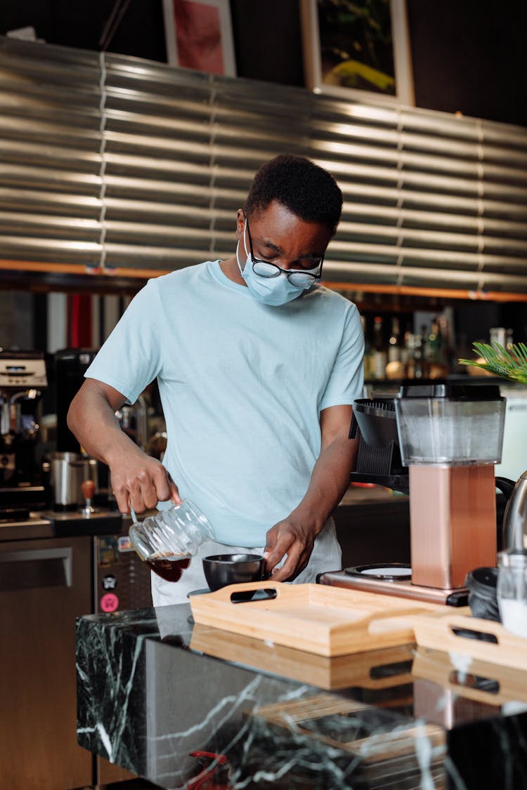 Man With Face Mask Pouring Coffee On A Black Cup