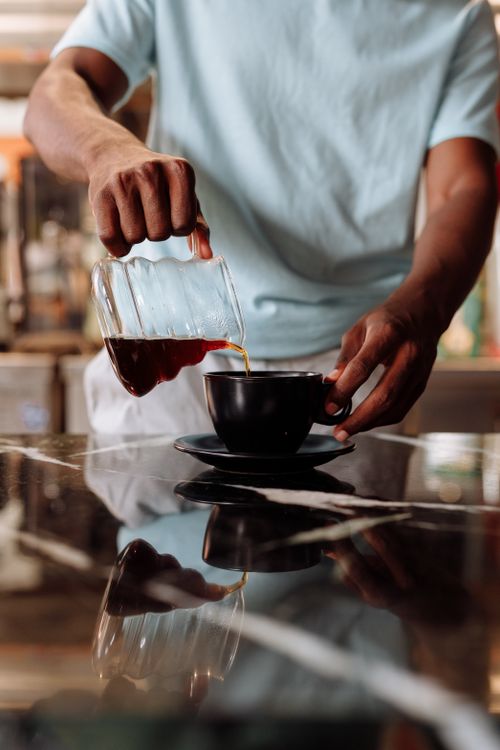 Free A person pours coffee into a cup on a reflective surface, capturing a moment of brewing perfection. Stock Photo
