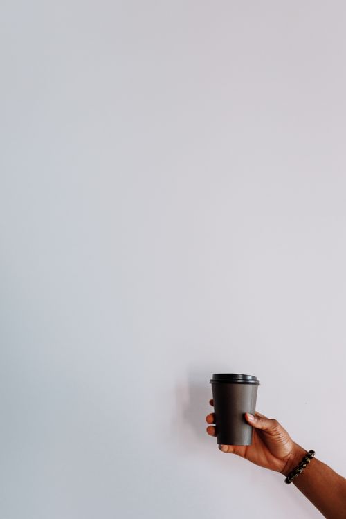 Free A simple and elegant shot of a person's hand holding a black coffee cup against a white wall. Stock Photo