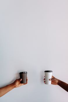 Two hands holding black and white coffee cups on a minimalist white background.