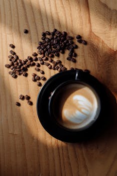 Top-down shot of a black cup latte with scattered coffee beans on a wooden table.