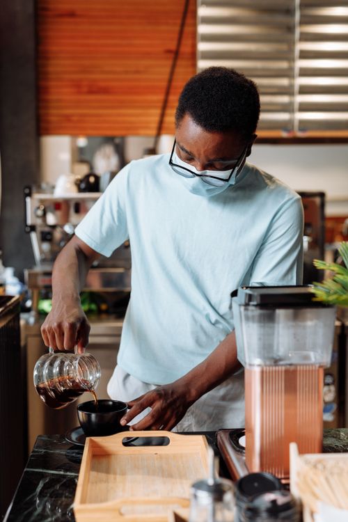 Free African American barista skillfully making pour-over coffee in a modern café setting. Stock Photo