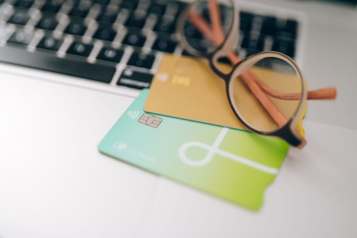 Dizüstü bilgisayar önünde kredi kartı tutan bir el finansal işlemi simgeliyor