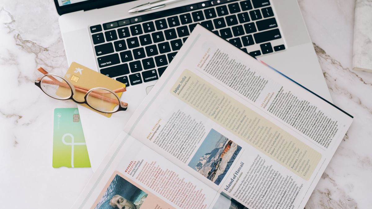 A laptop, credit card, and magazine laid out while booking a hotel