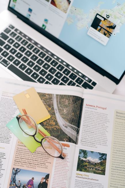 Open magazine with eyeglasses and cards next to a laptop, ideal for travel planning themes.