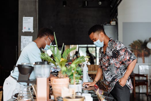 Barista and customer wearing masks at contemporary indoor cafe counter.