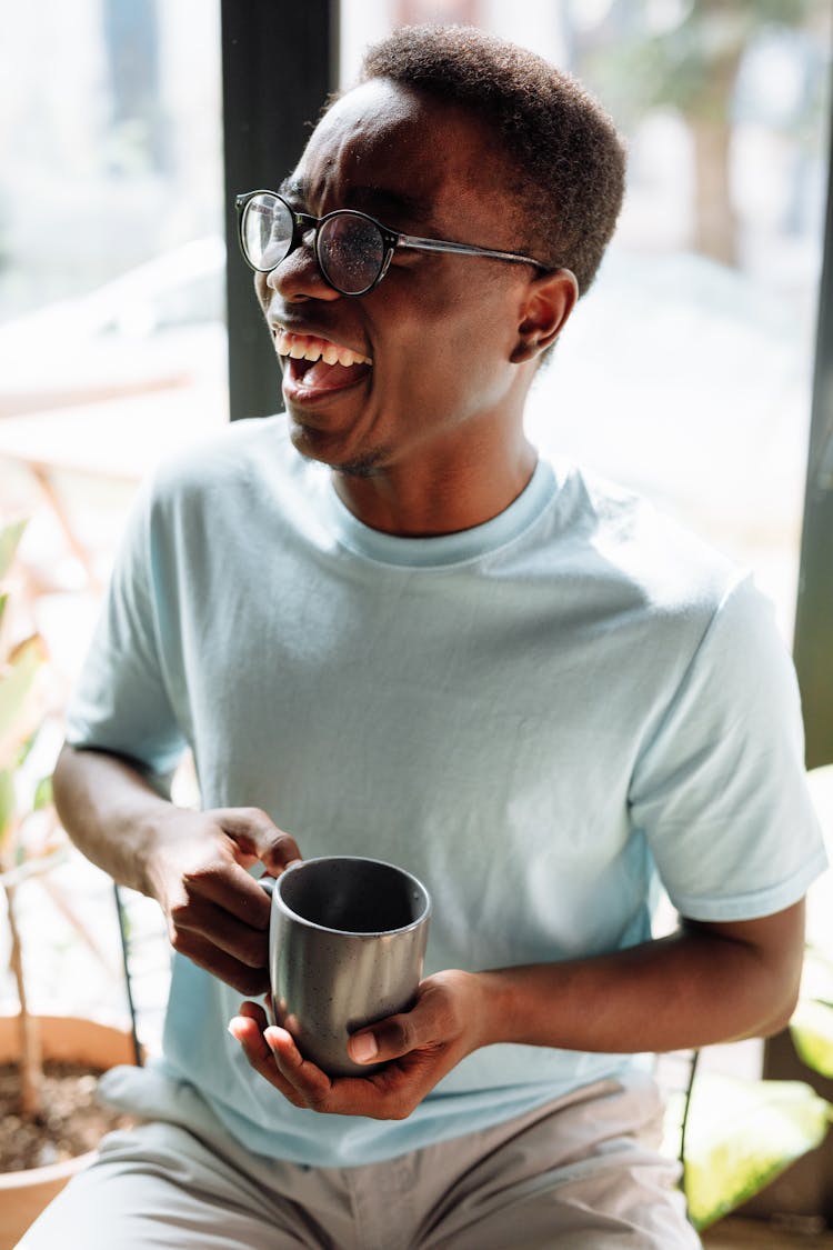 A Man Laughing While Holding A Cup Of Coffee