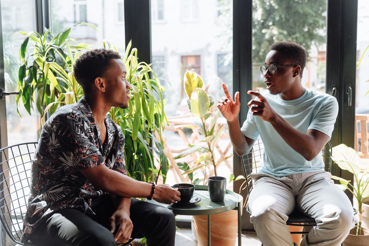 Two men in conversation at a cafe table by a sunlit window