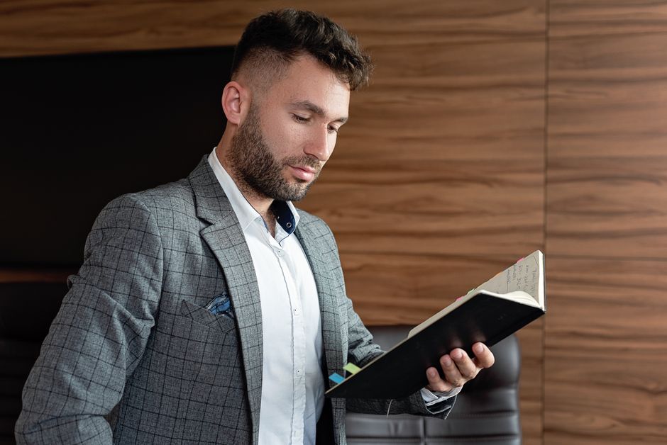 オフィスでノートを読んでいるプロのビジネスマンで、グレーのチェック柄のブレザーを着ています。