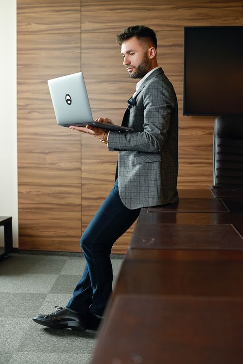 Free A man in a suit jacket stands in an office, holding a laptop and working. Stock Photo