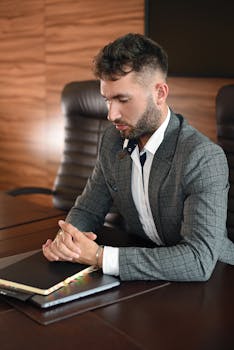 Young businessman in a gray suit contemplating at his office desk, focused and professional.