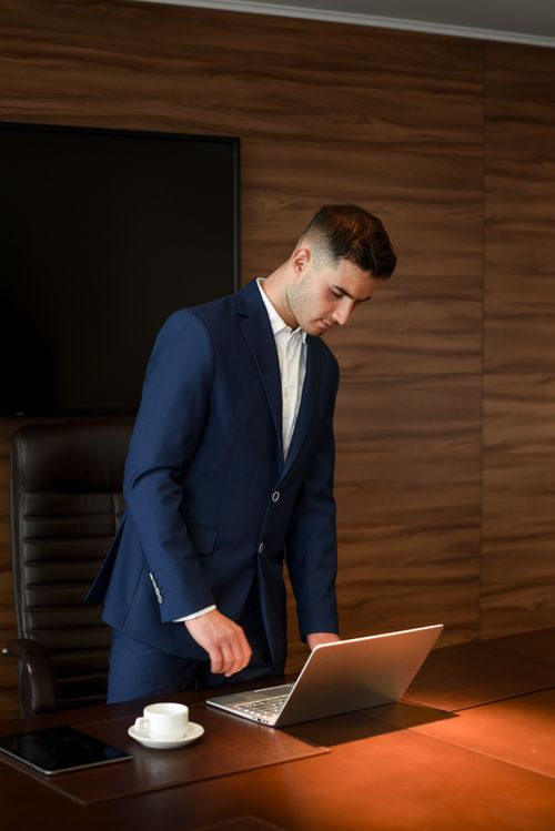 Free A young businessman in a blue suit works on a laptop in a modern office setting. Stock Photo