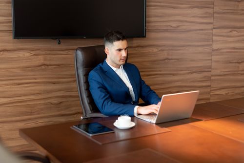 Free A focused businessman in a blue suit working on a laptop in a modern office setting. Stock Photo