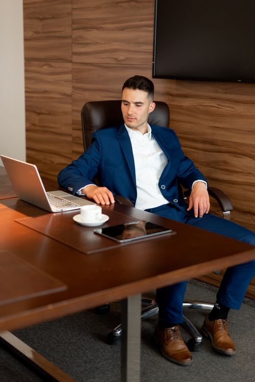 Free Confident young businessman in a suit working on a laptop at a wooden desk. Stock Photo