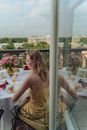 Woman in Brown Spaghetti Strap Dress Sitting on Chair in Front of Table