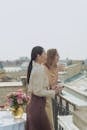 Woman in White Long Sleeve Shirt Holding White Ceramic Mug Standing Beside Woman in White Long