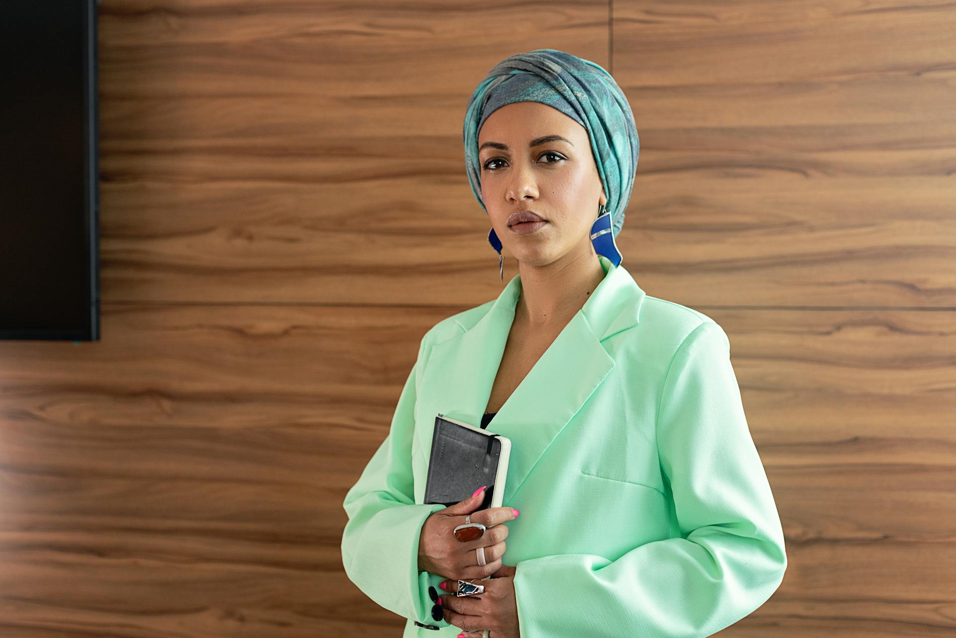 Elegant businesswoman posing indoors, holding an organizer, conveying professionalism and confidence.