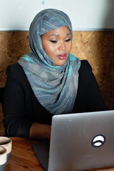 Confident businesswoman wearing a hijab and working on a laptop in an office setting.