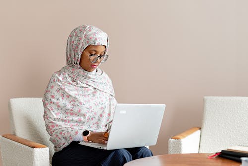 A Woman Sitting on the Chair while Typing on Her Laptop