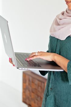Close-up of a woman wearing a hijab typing on a laptop indoors.