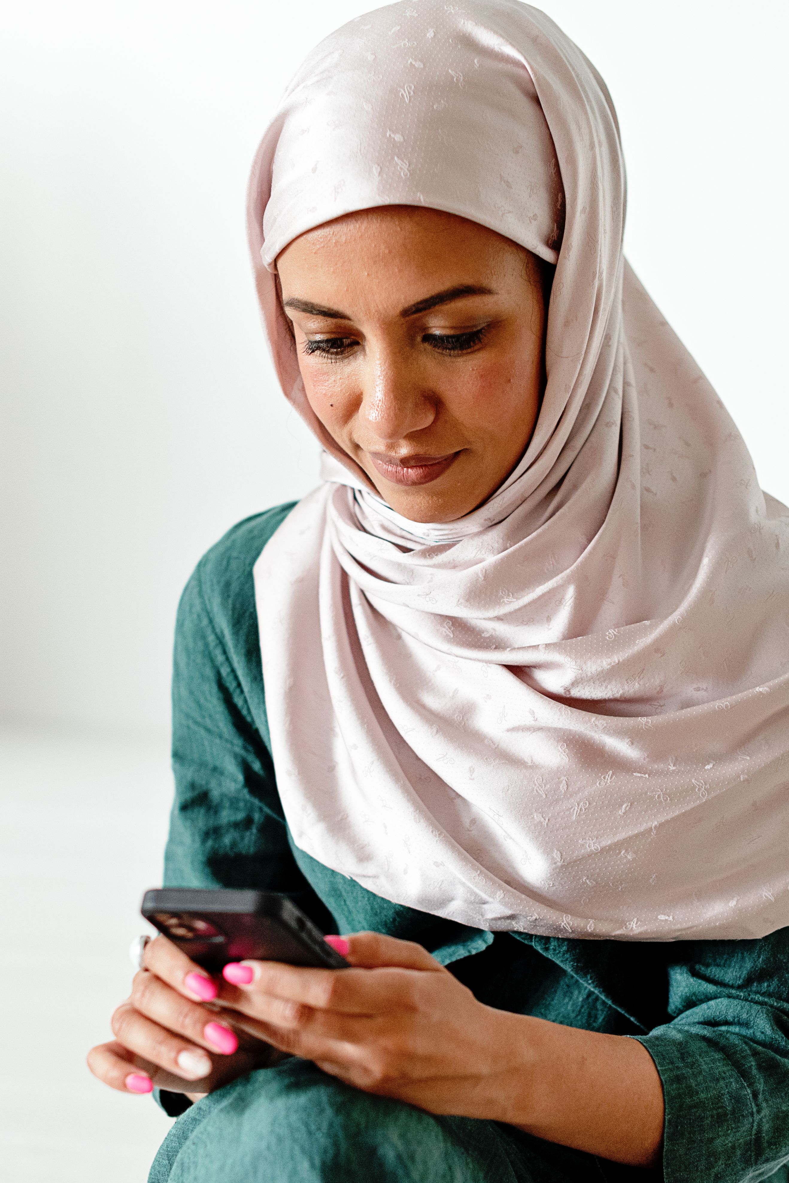 Woman in White Hijab Sitting and Using a Cell Phone · Free Stock Photo