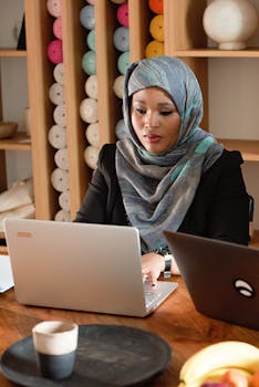 Businesswoman in hijab working at a laptop in a modern office setting.