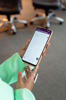 Elegant hands holding smartphone displaying app screen in modern office environment.