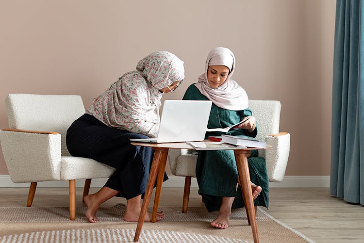 Women Sitting On Accent Chairs Looking At The Notebook 