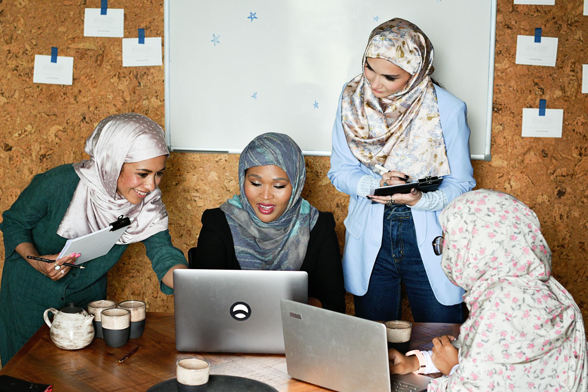 Four Muslim women in hijabs working together in a modern office setting, showing teamwork and diversity.