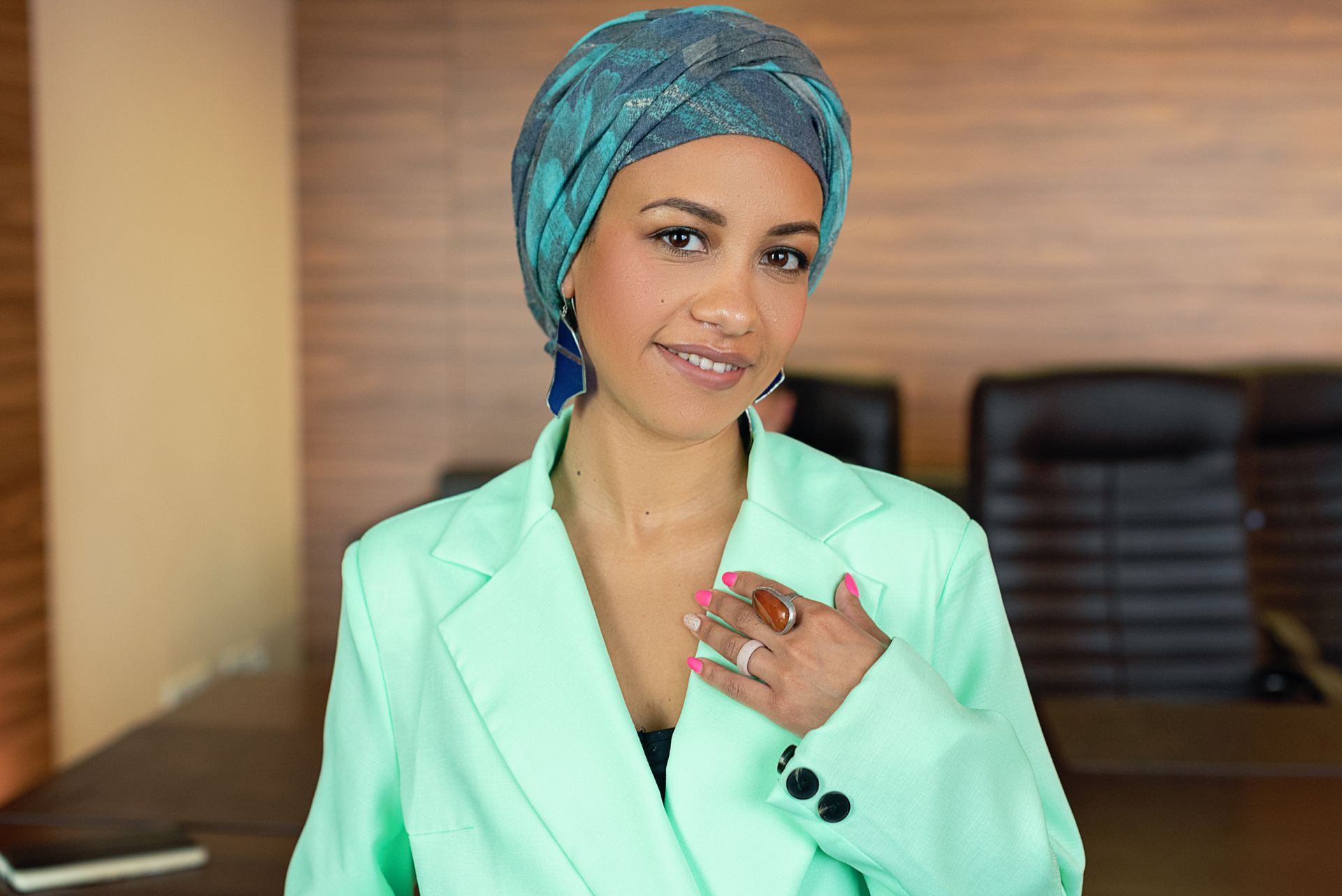 Portrait of a smiling businesswoman wearing a fashionable headscarf and pastel blazer in an office setting.