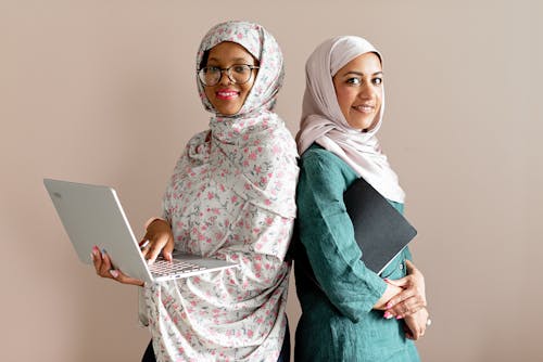 Woman Holding a Laptop Beside a Woman Holding a Notebook
