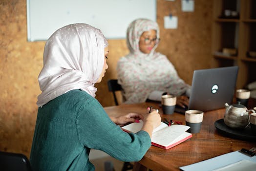 Muslim women in hijabs working and writing notes in a modern office setting.
