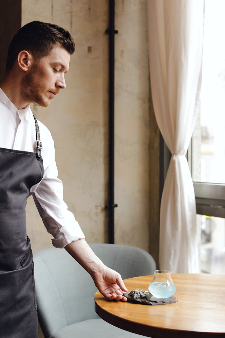 Waiter In Black Apron Putting Drink On The Table 