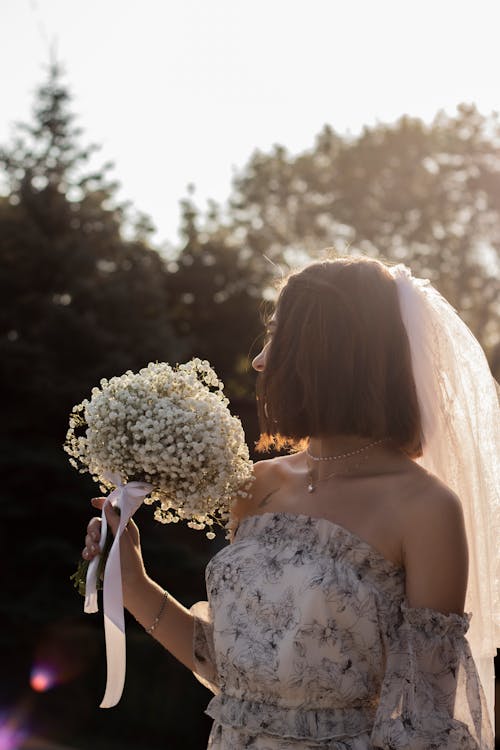 Free Woman Wearing White Floral Dress Holding Bouquet of Flowers Stock Photo