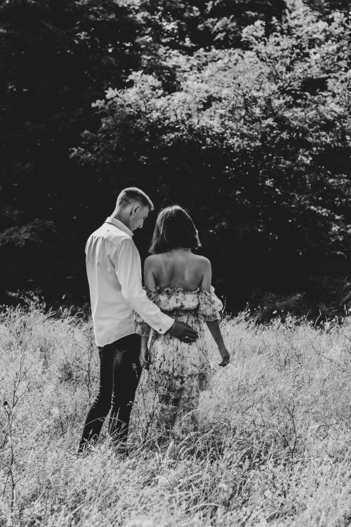 Free Black and white image of a couple in love standing in a field, embracing amidst tall grass. Stock Photo